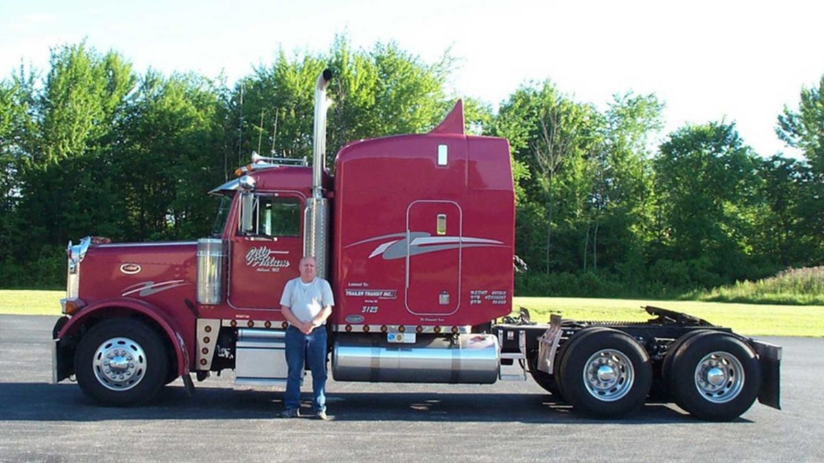 Trailer Transit Inc. | A man standing in front of a red semi truck.