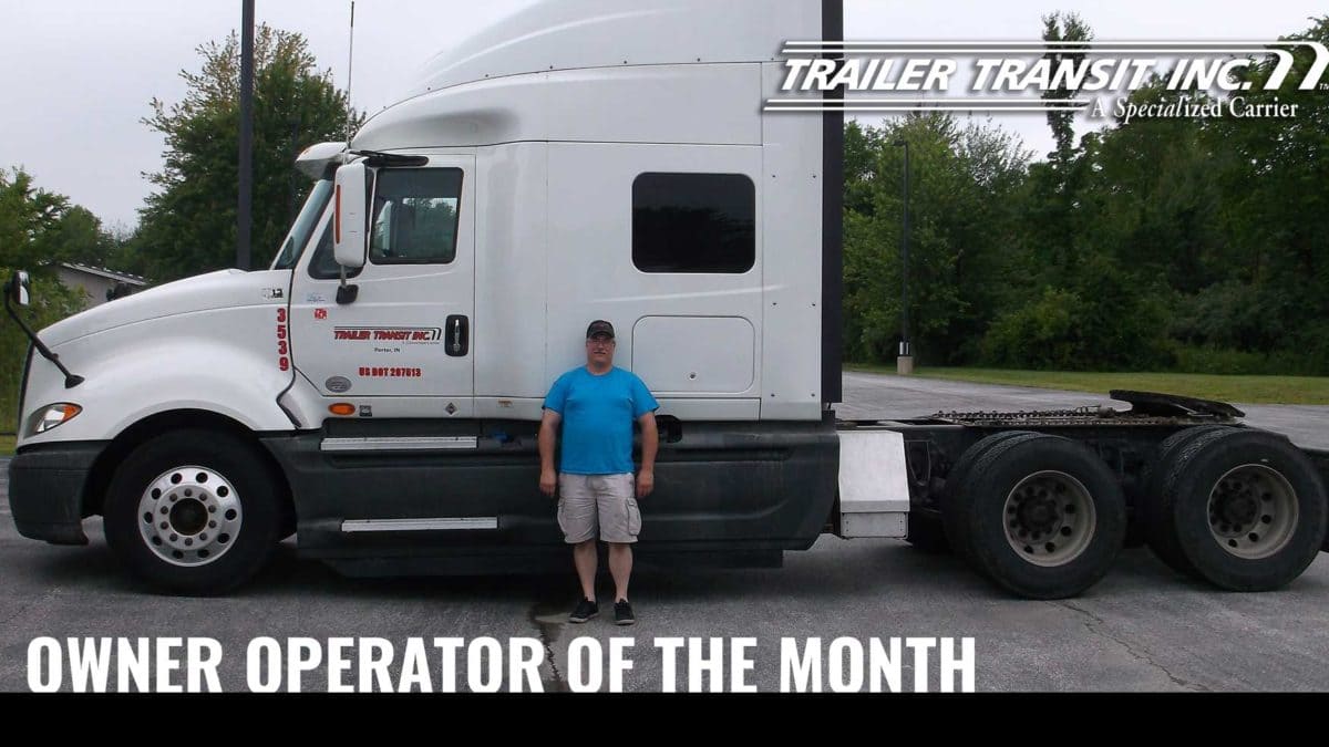 Trailer Transit Inc. | A man standing in front of a white semi truck with the words owner operator of the month.