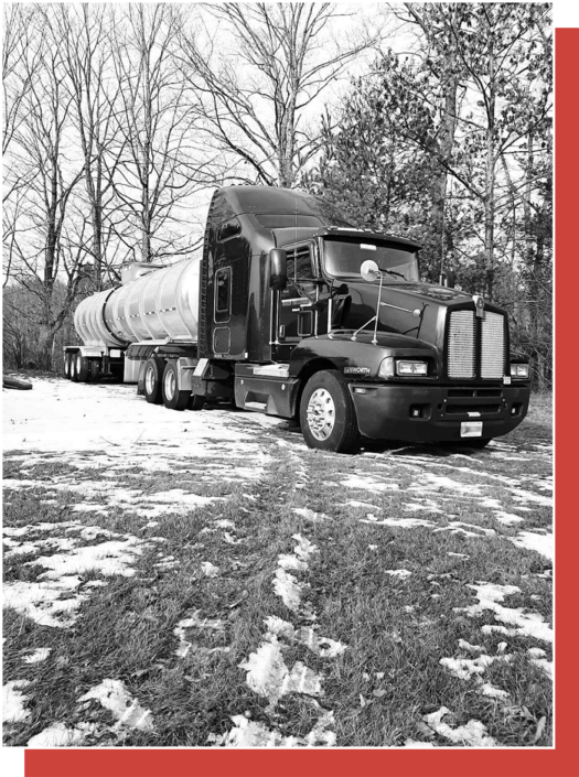 black and white image of Trailer Transit Inc. truck with tanker trailer parked near trees with snow on the grass