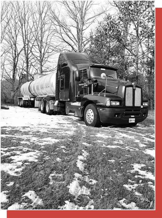 black and white image of Trailer Transit Inc. truck with tanker trailer parked near trees with snow on the grass