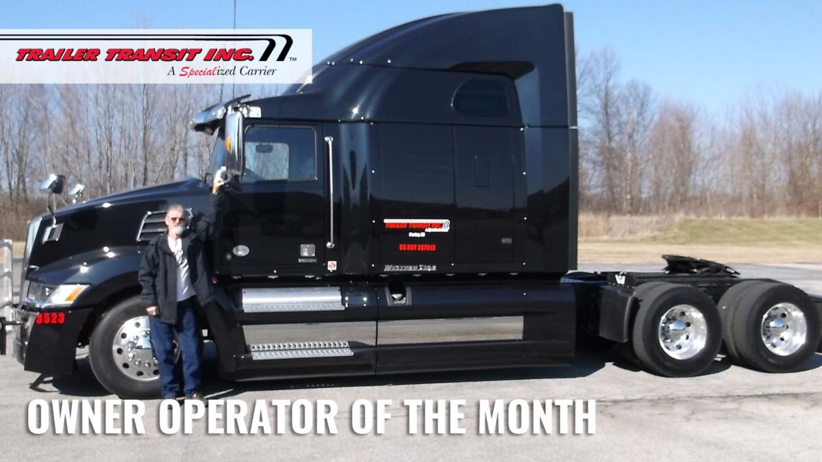 Trailer Transit Inc. | A man standing in front of a black semi truck with the words owner operator of the month.