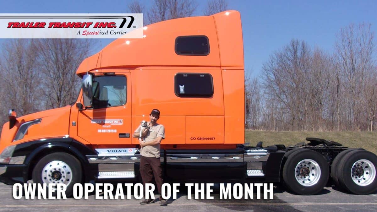 Trailer Transit Inc. | A man is standing in front of a large orange truck.