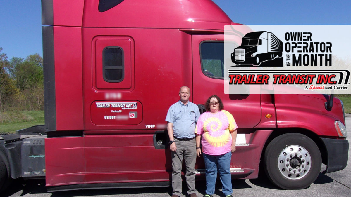 Trailer Transit Inc. | Two people standing in front of a red semi truck.