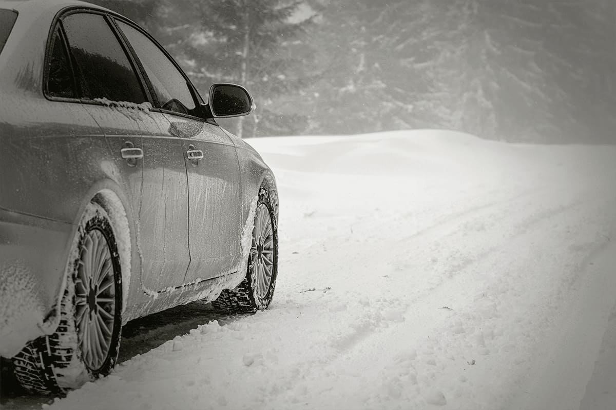 Silver car parked on snow covered road, detail view from behind, blurred trees background empty space for text right side