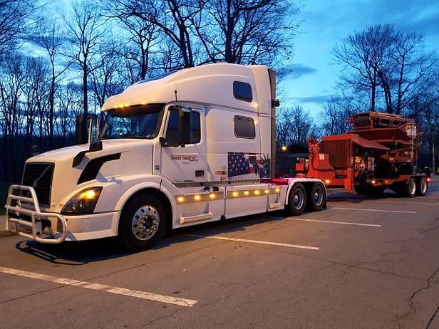 white semi truck hauling machinery