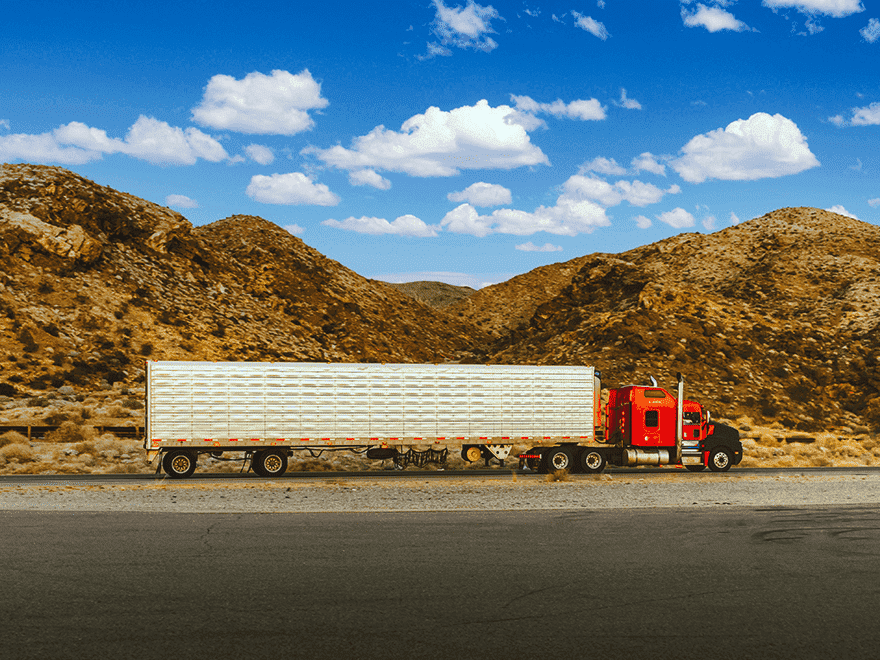 Trailer Transit Inc. | A semi truck owned by an operator driving down a road with mountains in the background.