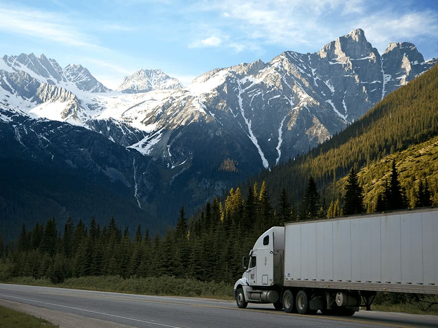 Trailer Transit Inc. | A semi truck owned by a transport company driving down a road with mountains in the background.