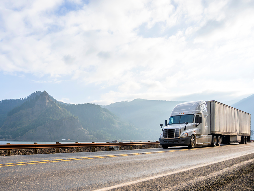 tractor trailer on the road with lake and mountians