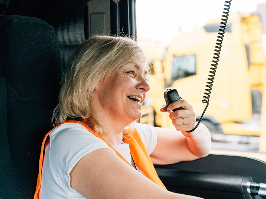 Female truck driver in cab, smiling while talking on the radio