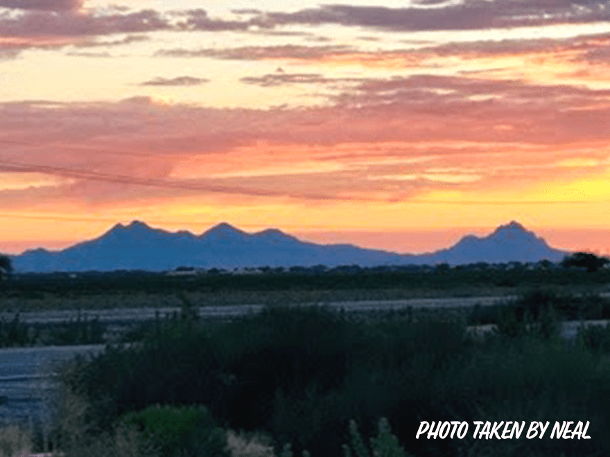 TT-BlogImage-1023-ArticleImages-2 Trailer Transit Inc. | Sunset with a sky painted in shades of orange and pink over distant mountain silhouettes, with "Photo taken by Neal, Owner Operator Transport Companies" text in the bottom right corner.
