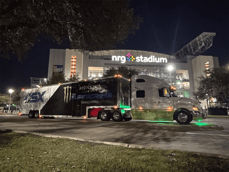 TT-BlogImage-1023-ArticleImages-3 Trailer Transit Inc. | A semi-truck with "Monster Energy Supercross" branding, owned by one of the top owner operator transport companies, is parked outside the illuminated NRG Stadium at night.