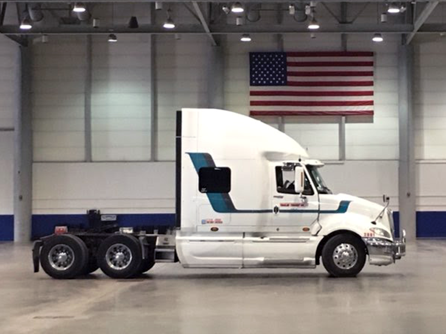 Trailer Transit Inc. | Power Only driver Neal's striped white semi truck parked in a warehouse with an American flag.