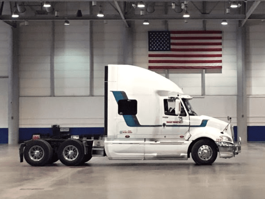 TT-BlogImage-1023-ArticleImages-4 Trailer Transit Inc. | Power Only driver Neal's striped white semi truck parked in a warehouse with an American flag.