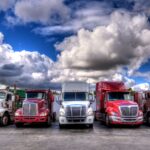 Trailer Transit Inc. | Several owner operator transport companies parked their trucks in a lot under the cloudy sky.