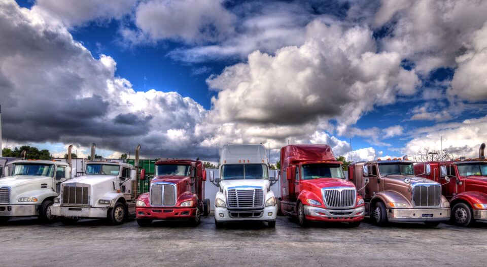 Trailer Transit Inc. | Several owner operator transport companies park their trucks in a lot under the cloudy sky.
