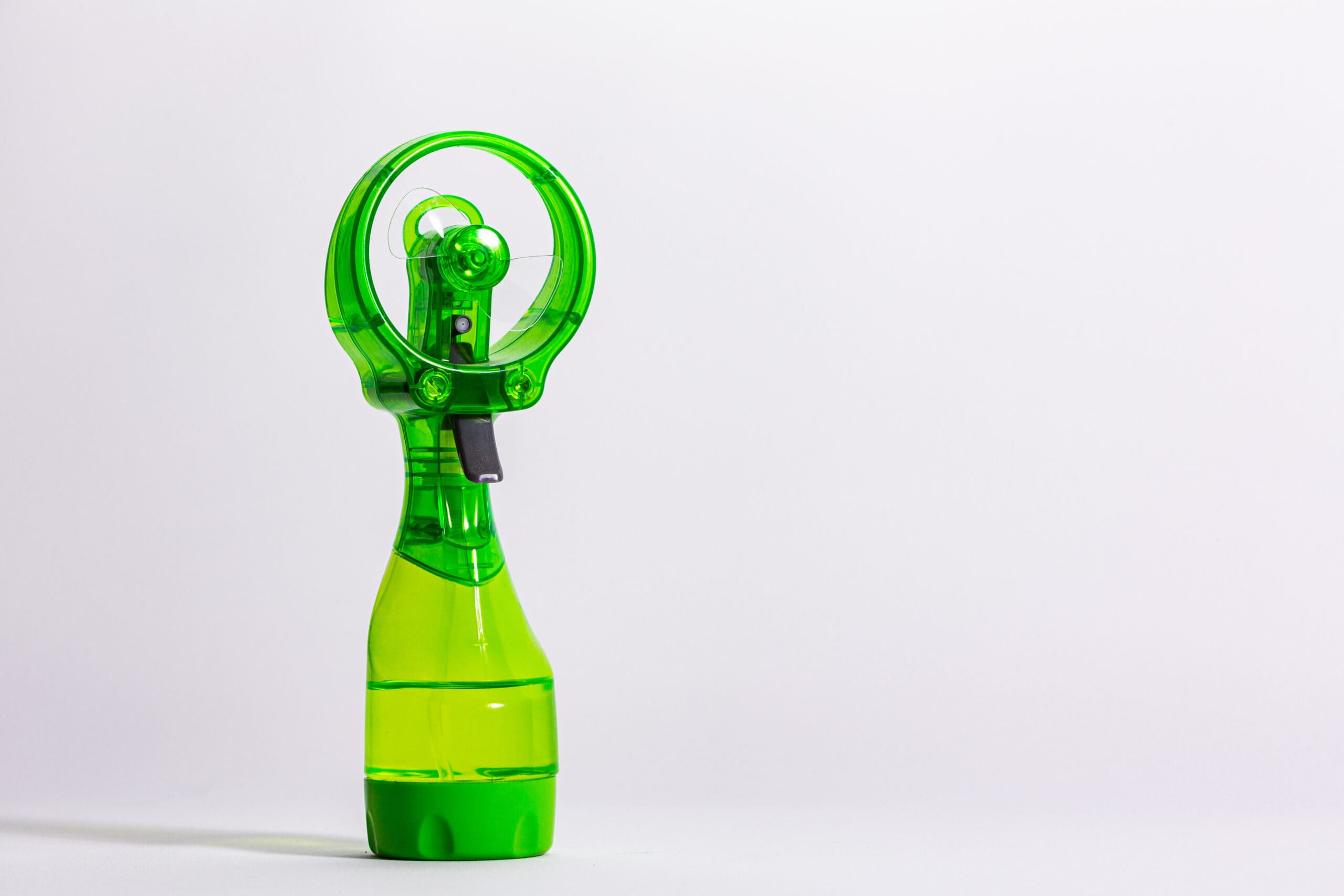 hand held water bottle mister with battery powered fan Trailer Transit Inc. | A small, green handheld misting fan with a circular guard and a water reservoir.