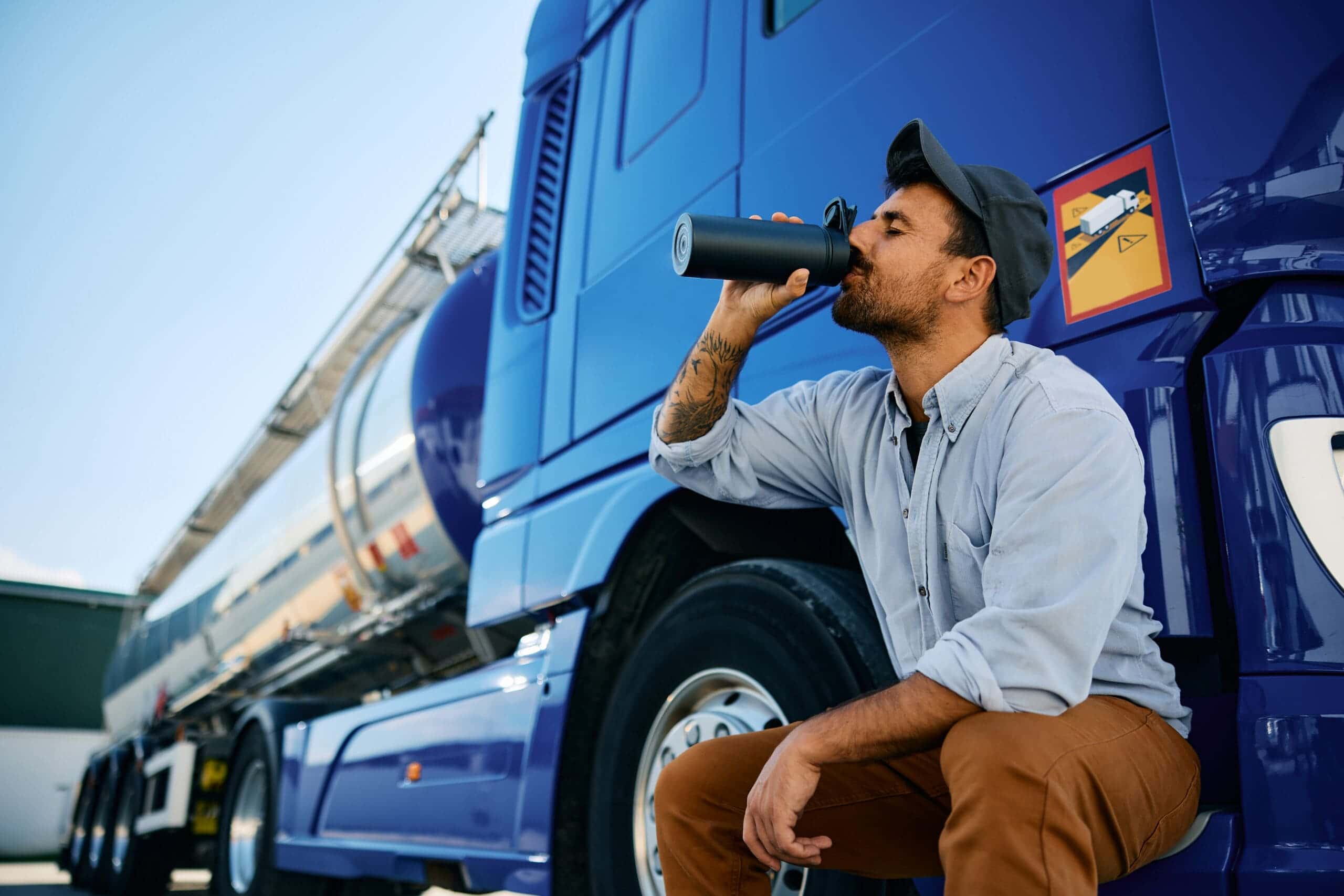 Truck driver drinking water from bottle on parking lot. Trailer Transit Inc. | A truck driver drinking water outside his rig.