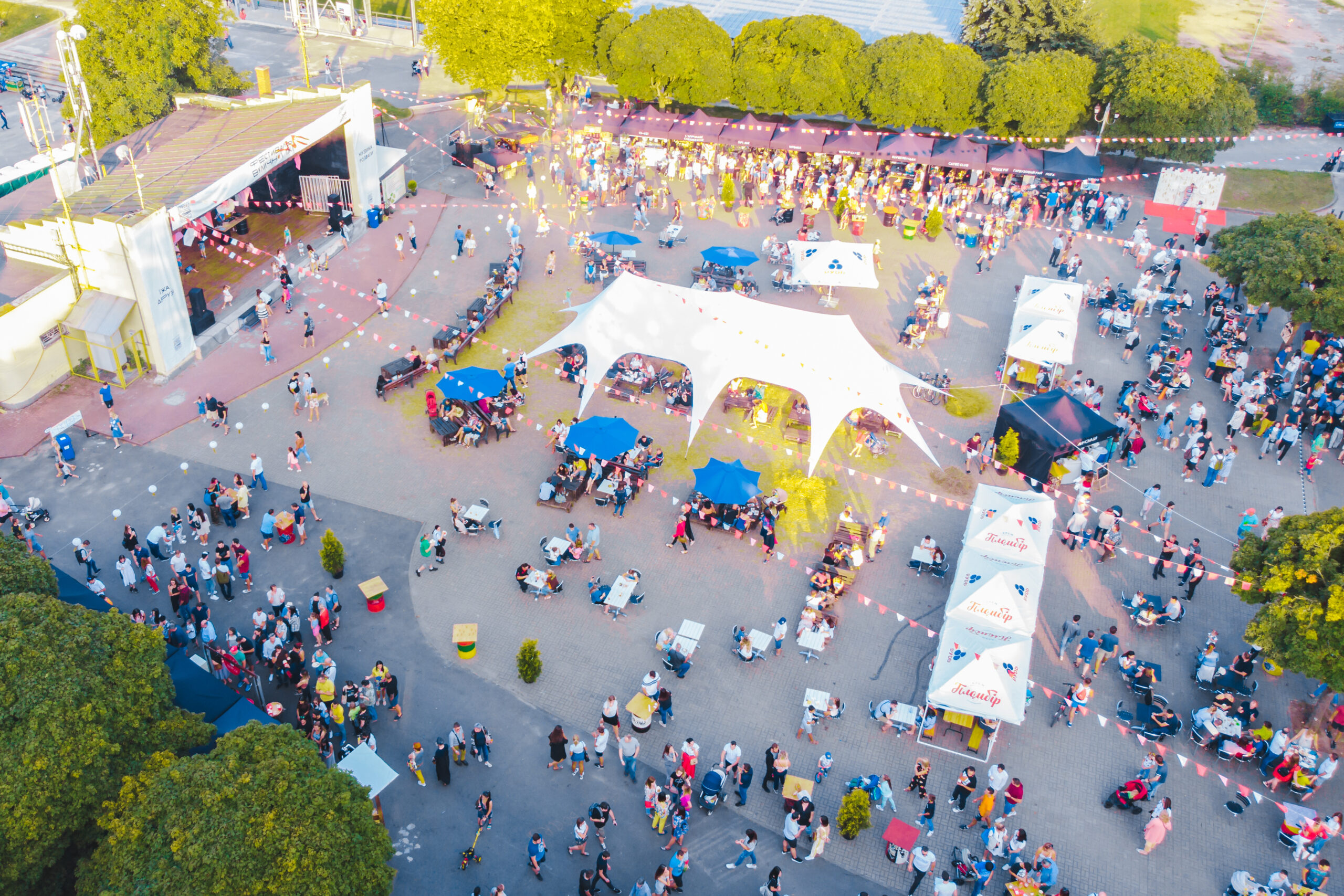 Trailer Transit Inc. | Aerial view of a busy outdoor festival with tents, stalls, and numerous people gathered around for food and live music.