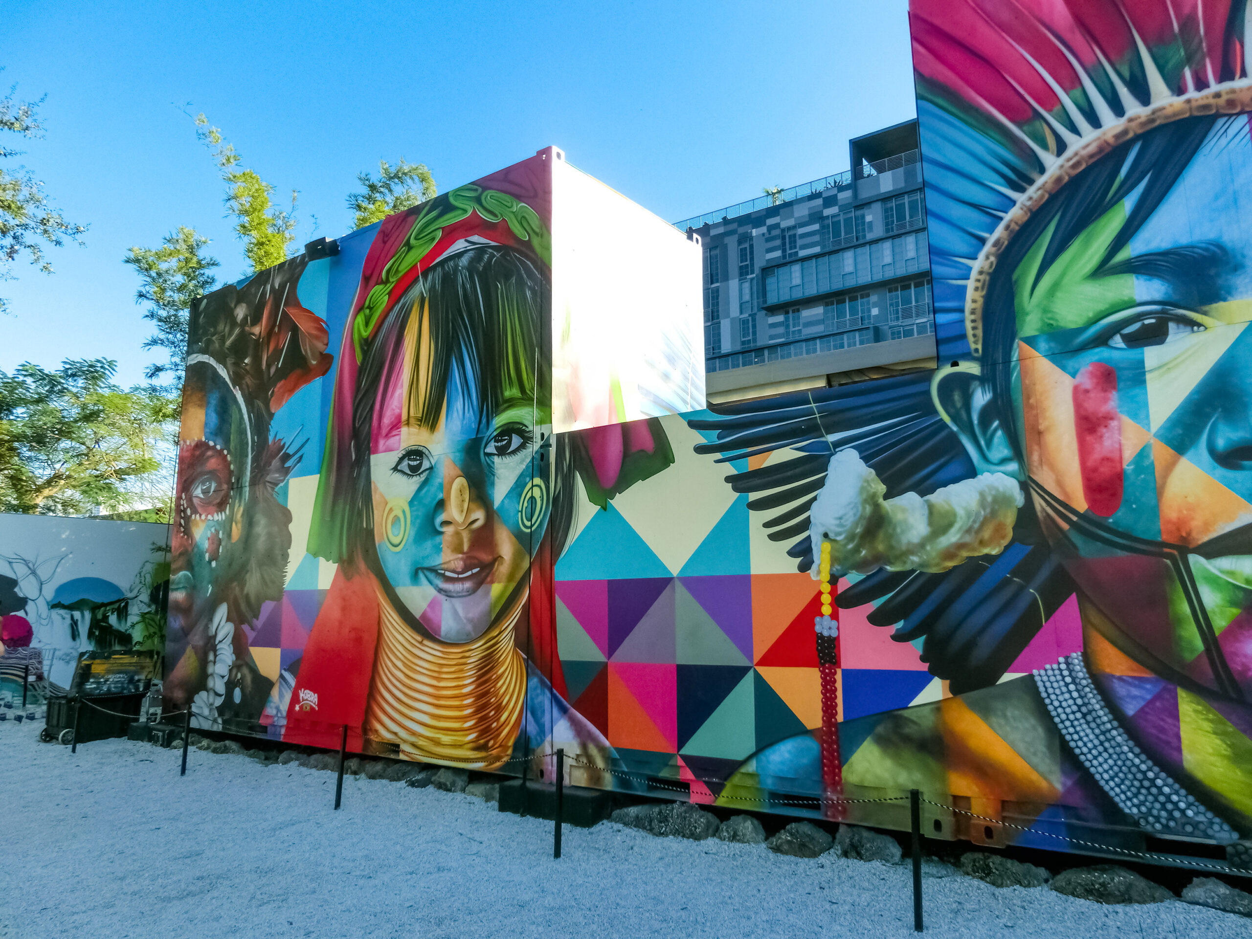 Trailer Transit Inc. | Colorful murals depicting faces of indigenous people adorned on large panels in an outdoor setting, with a building and trees in the background