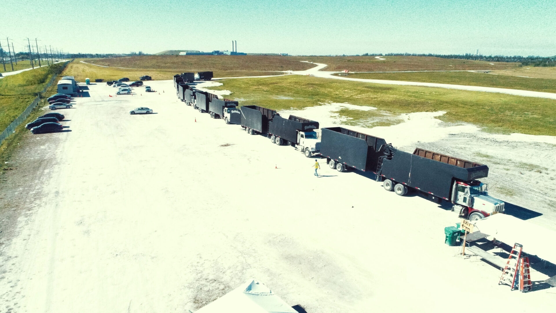 TANDEM DUMP TRUCK CARAVAN, CERTIFICATION PROCESSING, 2017 HURRICAN IRMA CLEAN-UP MIAMI. FEMA. Trailer Transit Inc. | A row of black dump trucks pulled by semi trucks are lined up at a disaster relief command site.