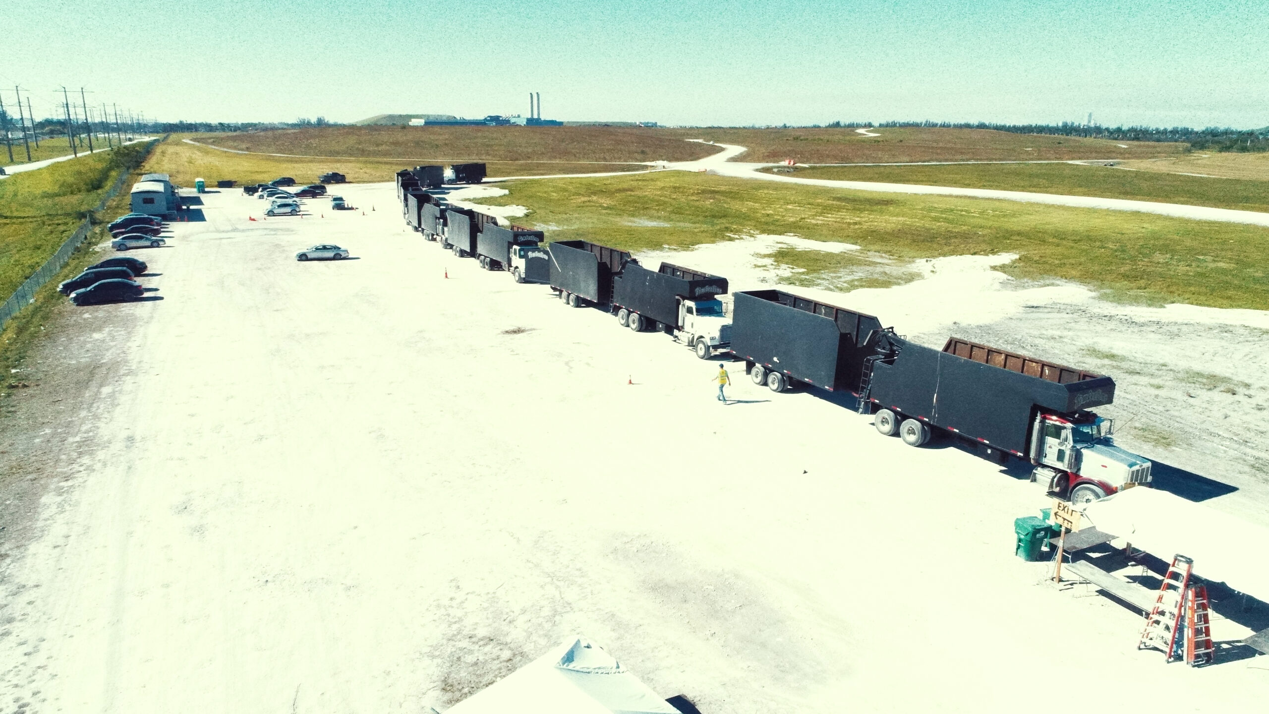 TANDEM DUMP TRUCK CARAVAN, CERTIFICATION PROCESSING, 2017 HURRICAN IRMA CLEAN-UP MIAMI. FEMA. Trailer Transit Inc. | A row of black dump trucks pulled by semi trucks are lined up at a disaster relief command site.