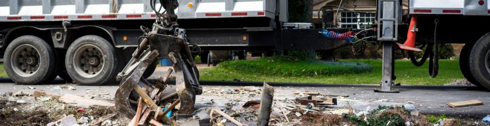haul Trailer Transit Inc. | A mechanical claw attached to a disaster relief trailer pulled by an owner operator, lifts debris and wooden planks from the ground on a residential street.