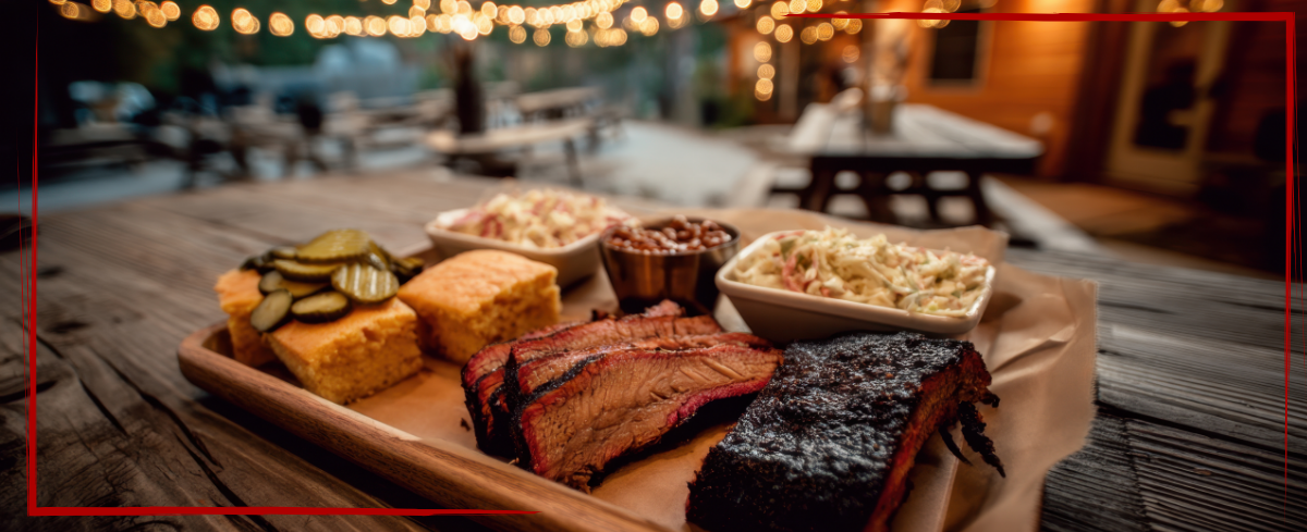 Trailer Transit Inc. | Texas BBQ including sliced brisket, cornbread, pickles, beans, and coleslaw sits on a wooden outdoor table under string lights - a favorite of many long-haul owner operators.