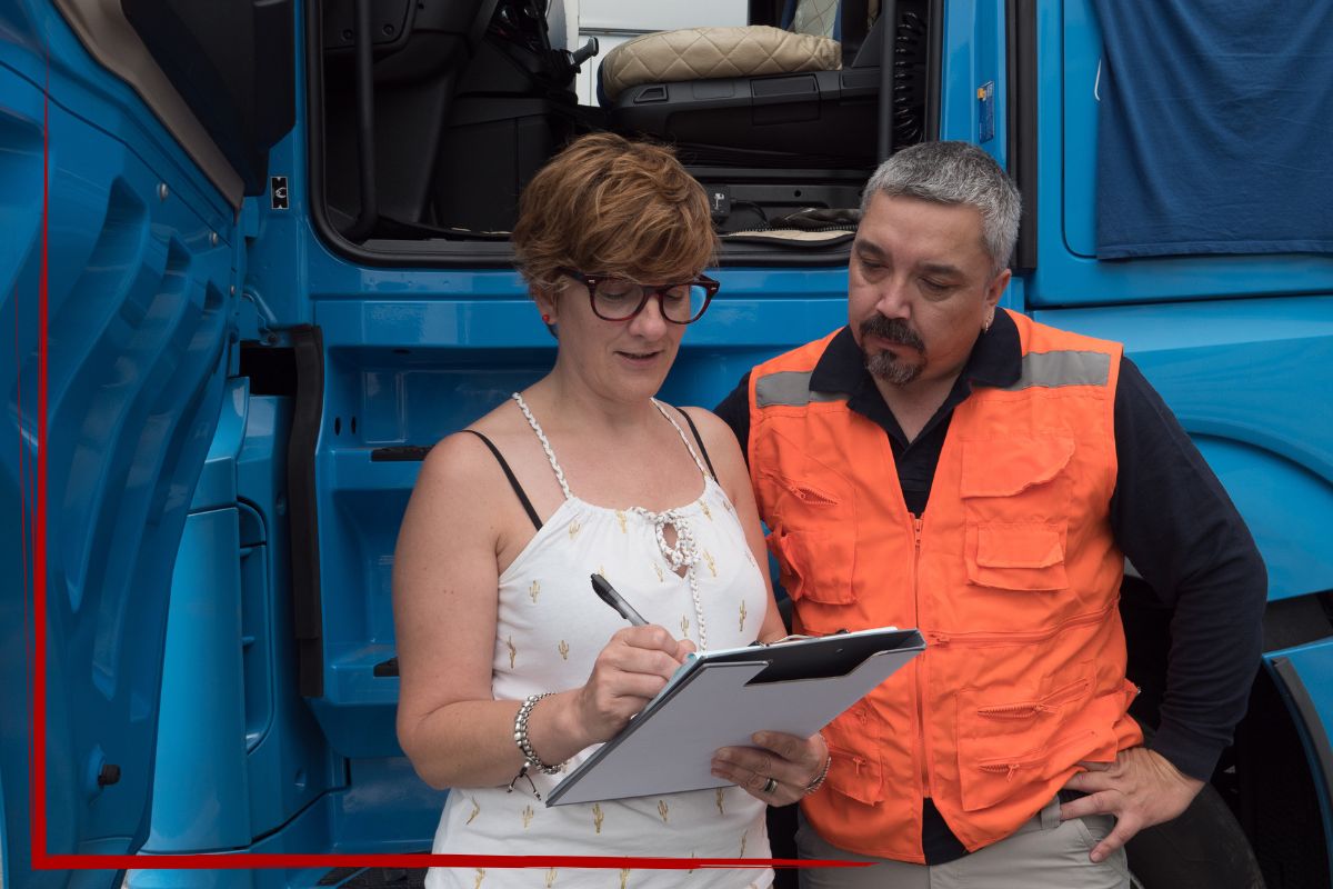Trailer Transit Inc. | A woman completes passenger paperwork while her husband, an owner operator in an orange vest, stands beside her in front of a blue truck.