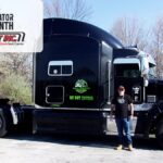 Trailer Transit Inc. | Owner Operator of the Month, Robert, stands in front of his black semi-truck parked outdoors, proudly recognized as Owner Operator of the Month by Trailer Transit Inc., with a sign in the corner celebrating his achievement.