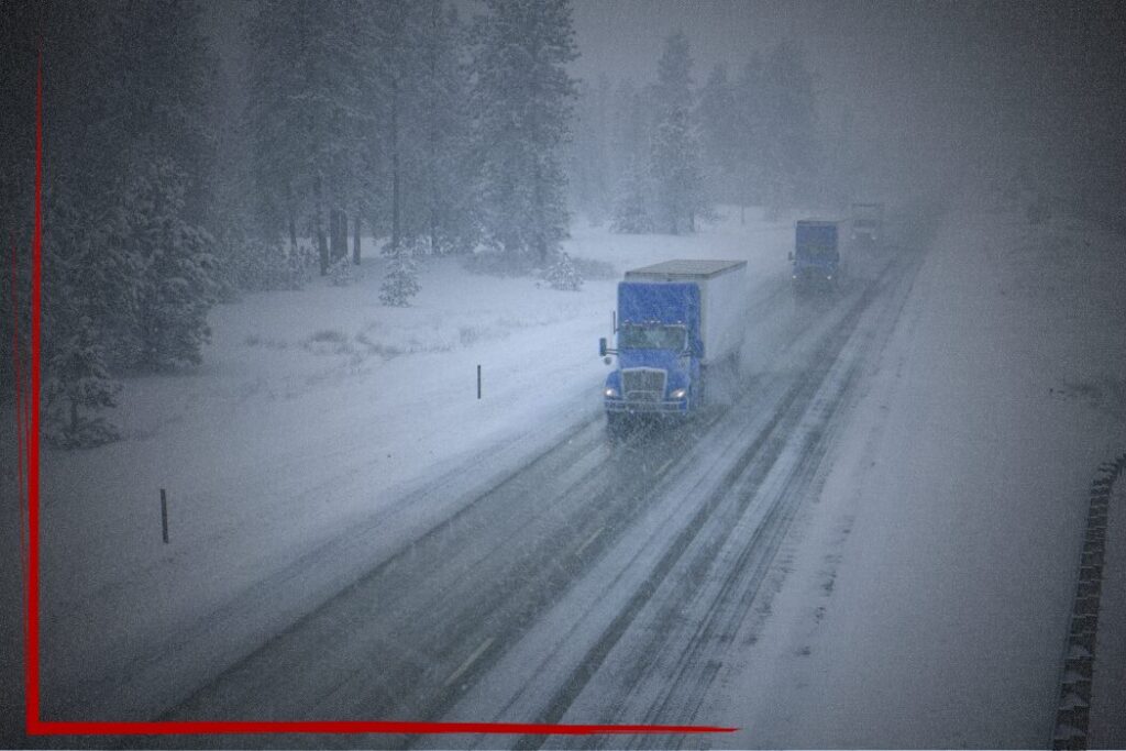 0126 Blog-2 Trailer Transit Inc. | Three semi trucks drive along a snow-covered highway in low visibility during a winter storm, highlighting the resilience of power-only trucking with a companion through challenging conditions, with trees and roadside barriers visible.