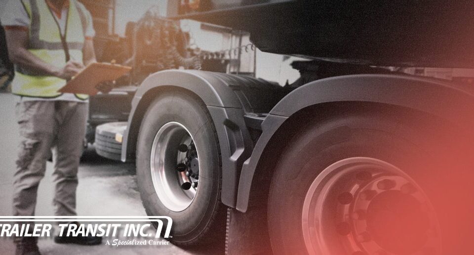 Trailer Transit Inc. | An Owner Operator holding a clipboard inspects his rig, carefully reviewing a truck and trailer maintenance checklist so he's prepared for seasonal hauls; the Trailer Transit Inc. logo is visible in the lower left corner.