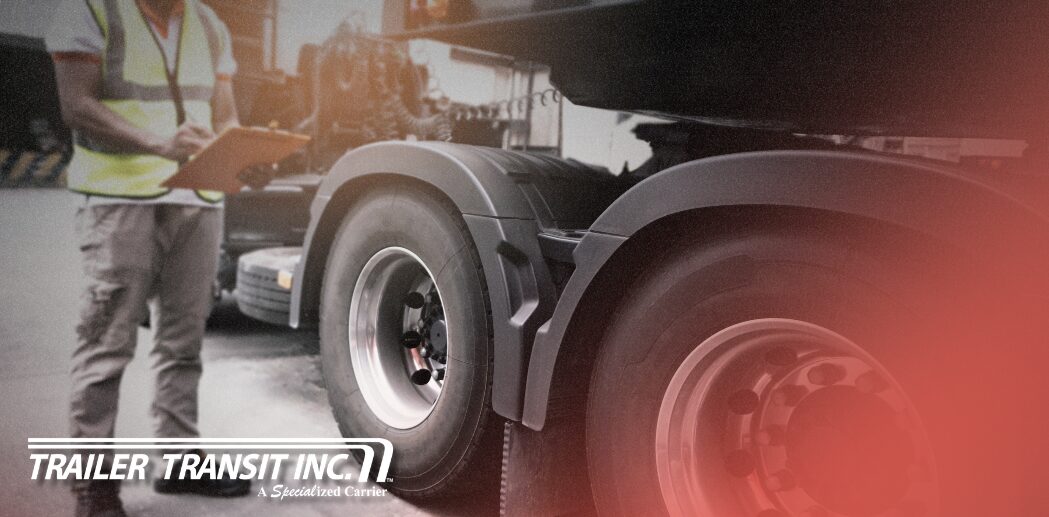 Trailer Transit Inc. | An Owner Operator holding a clipboard inspects his rig, carefully reviewing a truck and trailer maintenance checklist so he's prepared for seasonal hauls; the Trailer Transit Inc. logo is visible in the lower left corner.