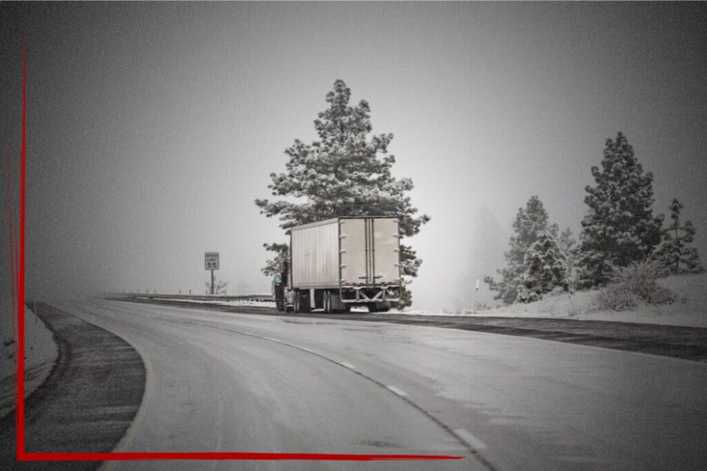 Trailer Transit Inc. | A semi-truck pulled over on a wet, snow-lined highway with pine trees and a speed limit sign visible in the background, illustrating how important it is to have a well-maintained truck during seasonal hauls.