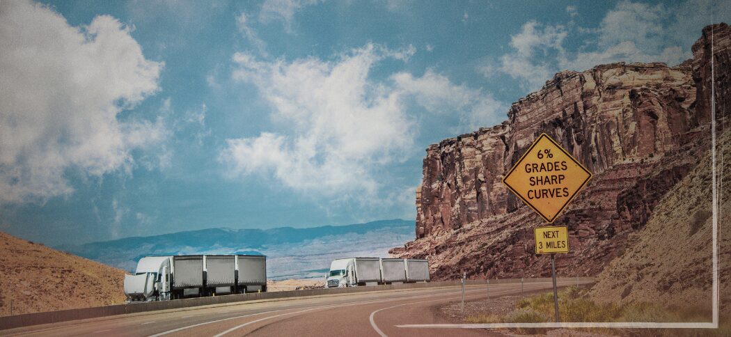 Trailer Transit Inc. | A semi-truck is pulled over with it's hood up on a winding highway through rocky terrain, another rig is passing, a road sign warning of a 6% grade and sharp curves for the next 3 miles, showing troubling situations that can result from not following a regular maintenance checklist.