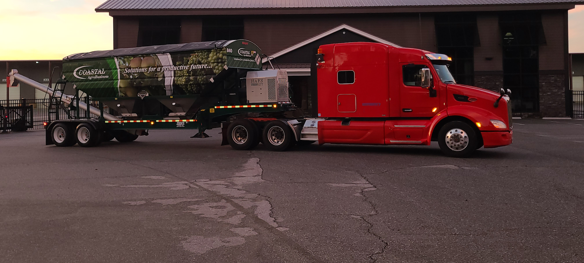 Trailer Transit, Inc. | A red semi-truck with a green Corbala Solutions trailer is parked on an asphalt lot in front of a building at dusk.