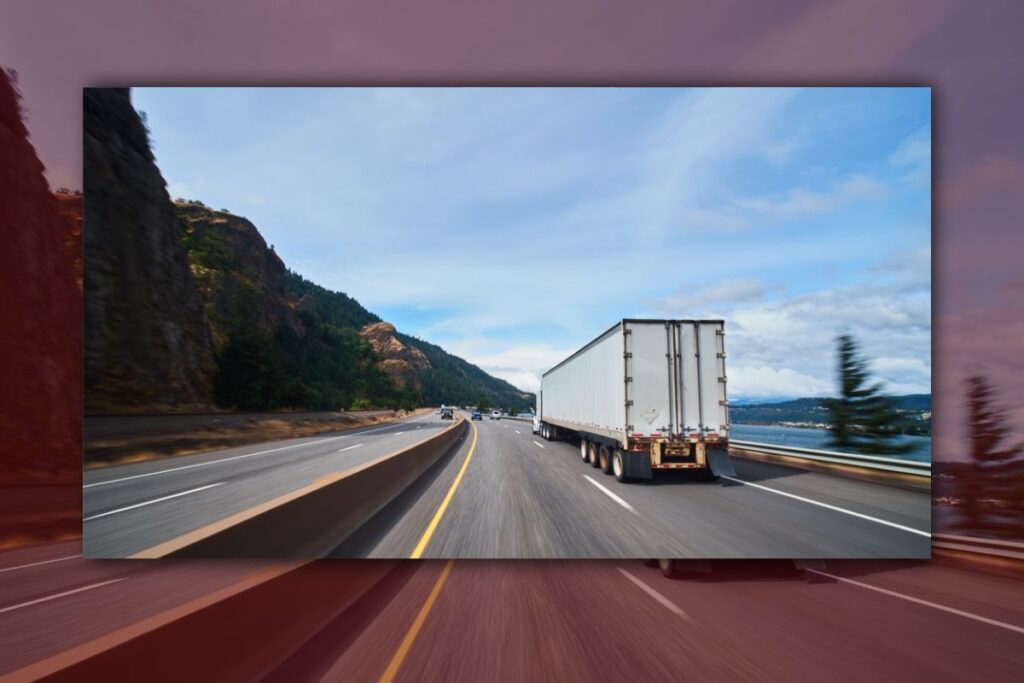 TT Blog - 0426-2 Trailer Transit Inc. | A semi-truck travels along a divided highway bordered by mountains and trees under a blue sky with scattered clouds, showing the reach of shipping when hiring power only truck transportation services.