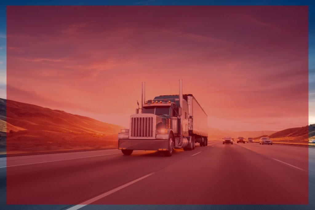 TT Blog - 0426-4 Trailer Transit Inc. | A semi-truck cruises down a multi-lane highway with hills in the distance and cars nearby with a red overlay—a demonstrating hiring truck transportation services.