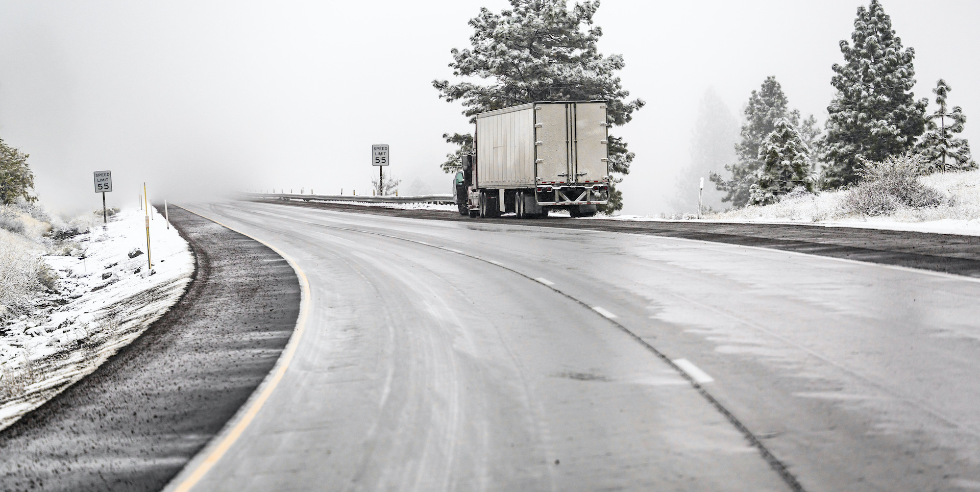 Broken big rig semi truck with open hood and dry van semi trailer standing out of service on the winding winter road with snowfall waiting for towing on mobile repair road service