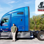 Trailer Transit, Inc. | Power Only driver, O.J. stands in front of his blue semi truck as the owner operator of the month of April. There are green trees in the background and the owner operator of the month logo overlay at the top.