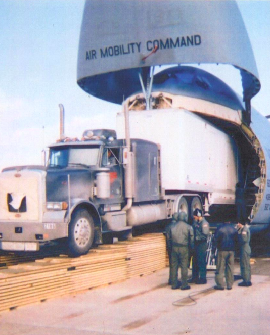 Trailer Transit, Inc. | A semi truck is being loaded into a large cargo aircraft labeled "Air Mobility Command" while four people in uniforms stand nearby.