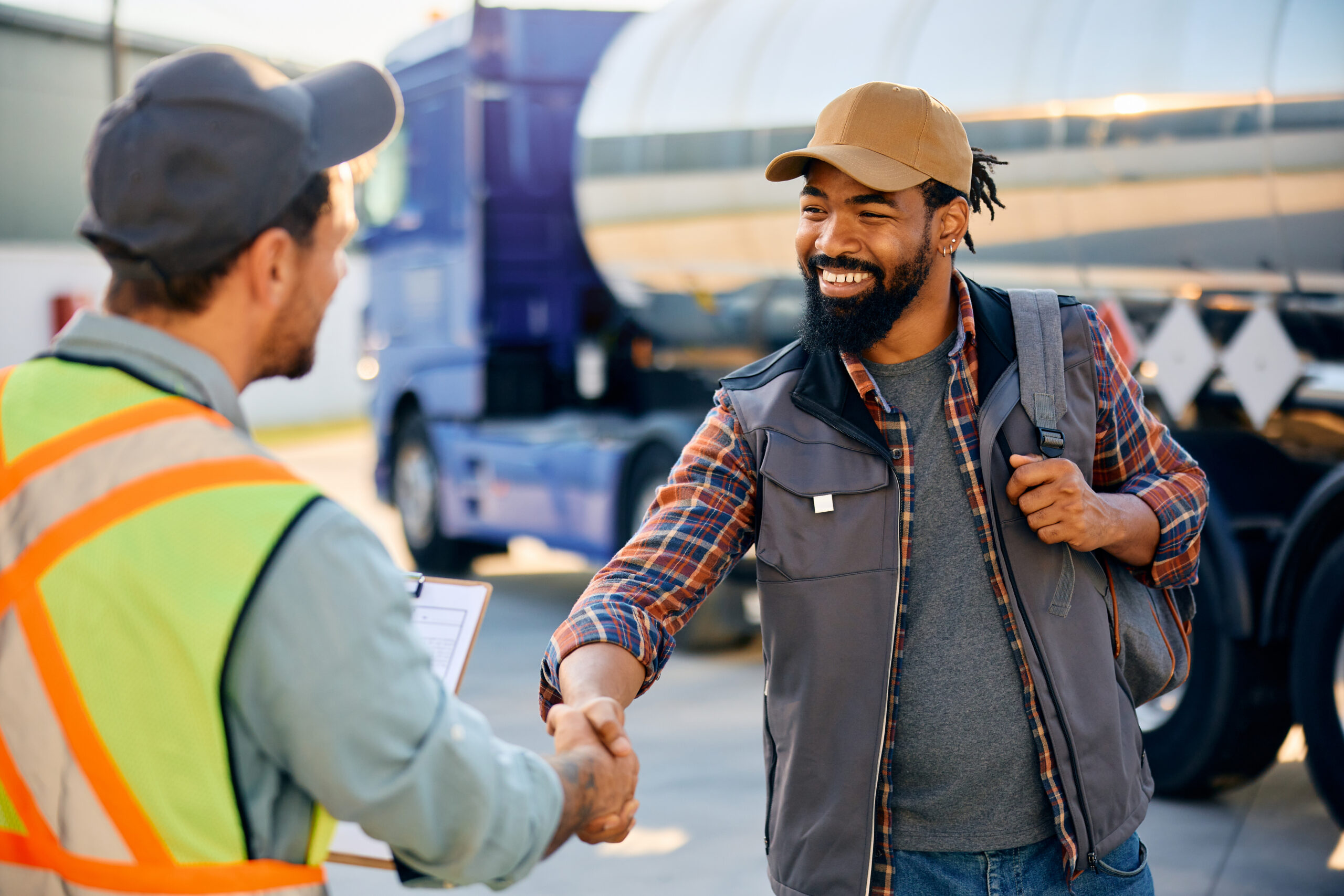Trailer Transit, Inc. | Two men, one in a safety vest and an owner operator in casual clothes with a cap and backpack, shake hands outdoors near a tanker truck.